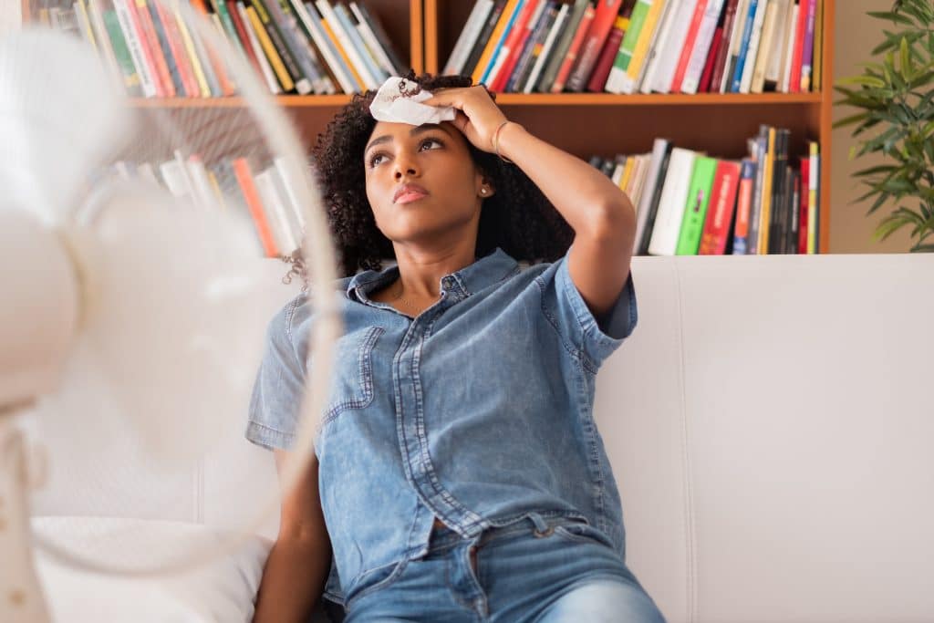 Woman sitting on her couch while wiping sweat off her forehead