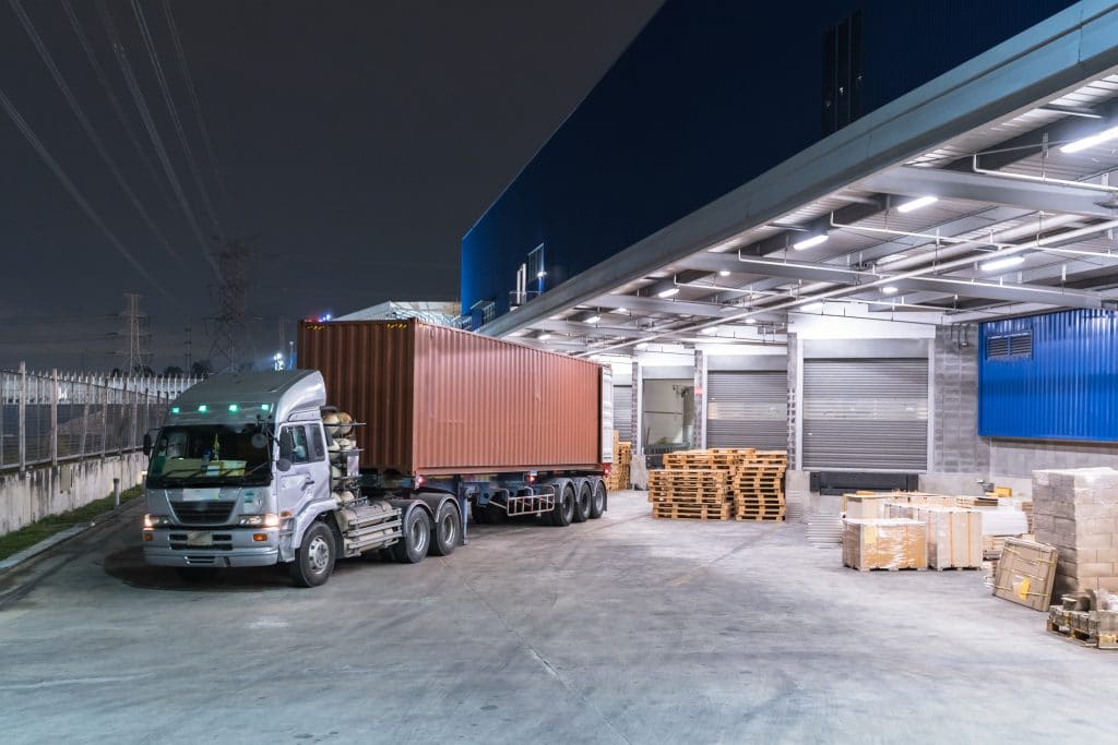 A freight truck loaded with a shipping container pulling out of a loading dock