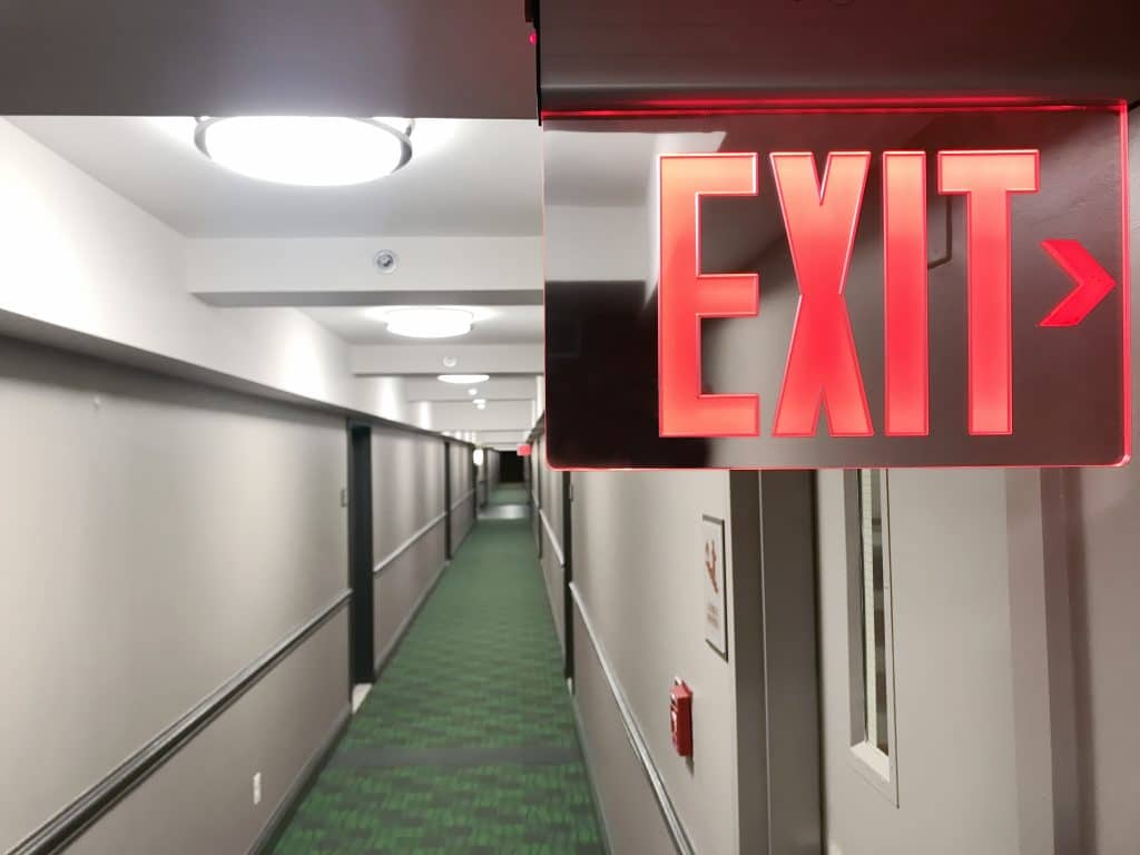 A fluorescent emergency exit sign in a hotel hall way