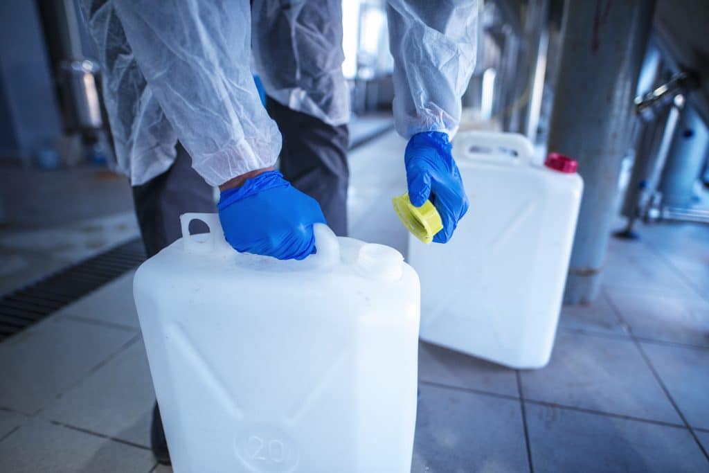 Person in a plastic suit adding cap to a bottle containing chemicals