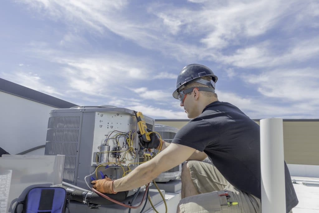 Professional on a rooftop repairing a HVAC unit as part of facilties management