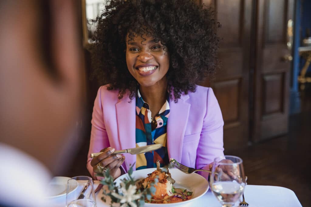 Woman smiling with plate of food while sitting at a restaurant dining room table 