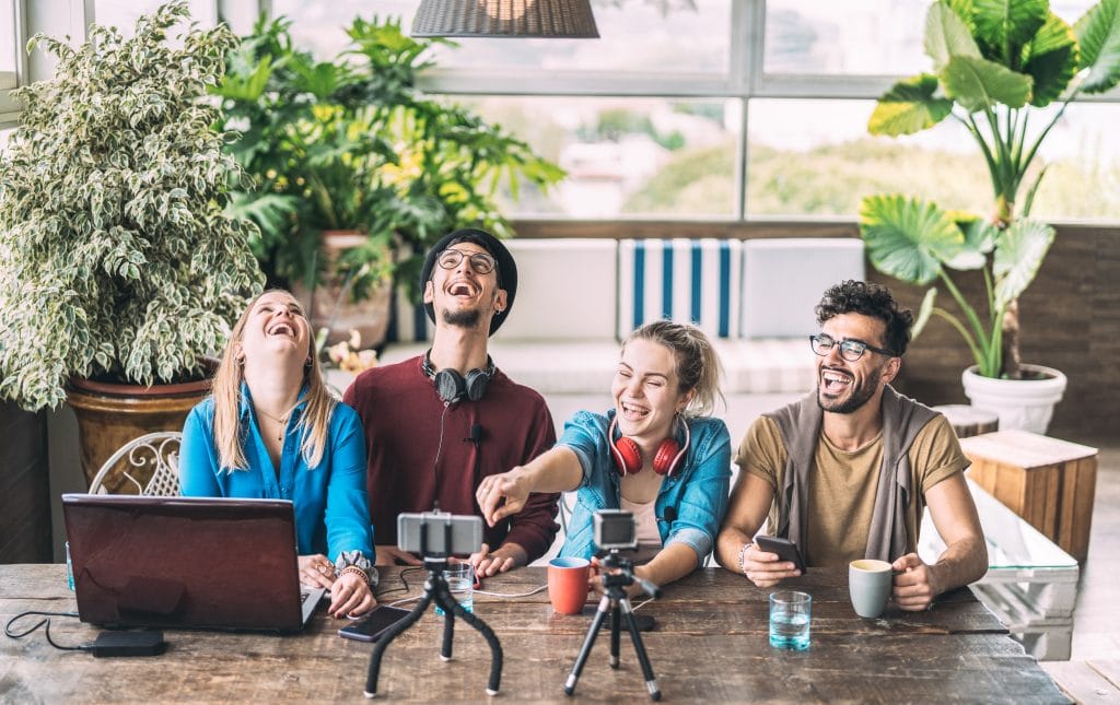 Group of Gen Z adults using various devices on a table inside a cafe