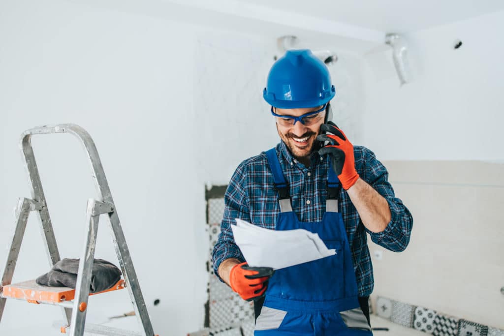 Professional home builder with a helmet at work talking to client on phone to ensure customer satisfaction