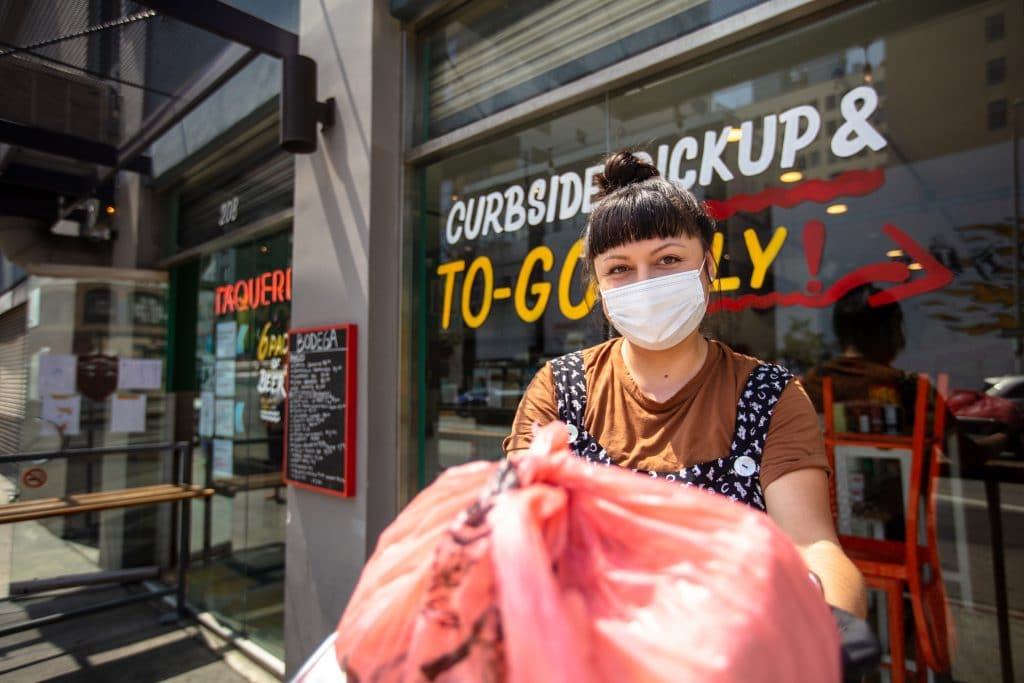 Female employee at a curbside pickup area handing food order to a customer