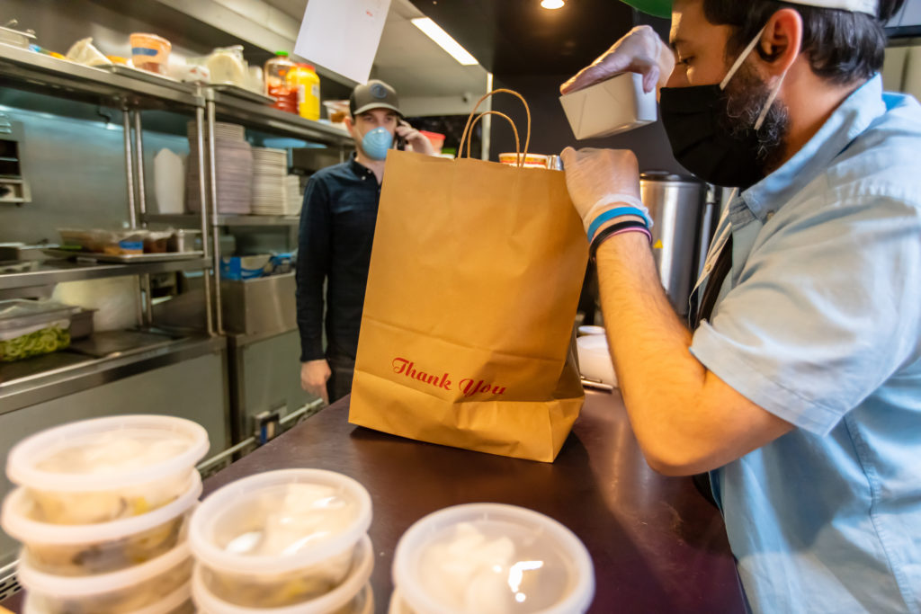 Ghost kitchen employee at a counter filling a bag with food orders 