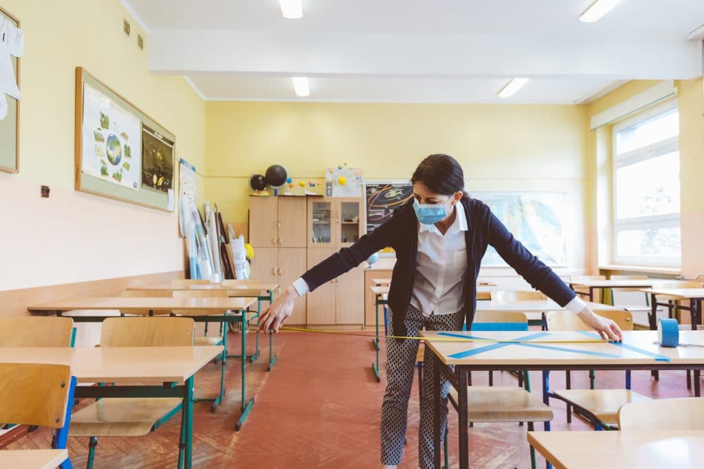 Woman measuring space for physical distancing between desks inside a classroom