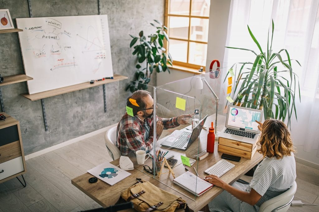 Office employees at a desk with a plastic separator between them