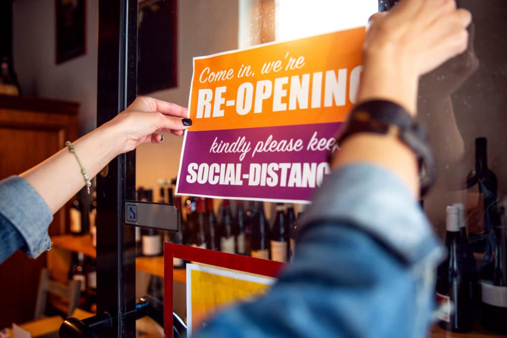 A person placing a sign on a door to to announce retail store openings after COVID