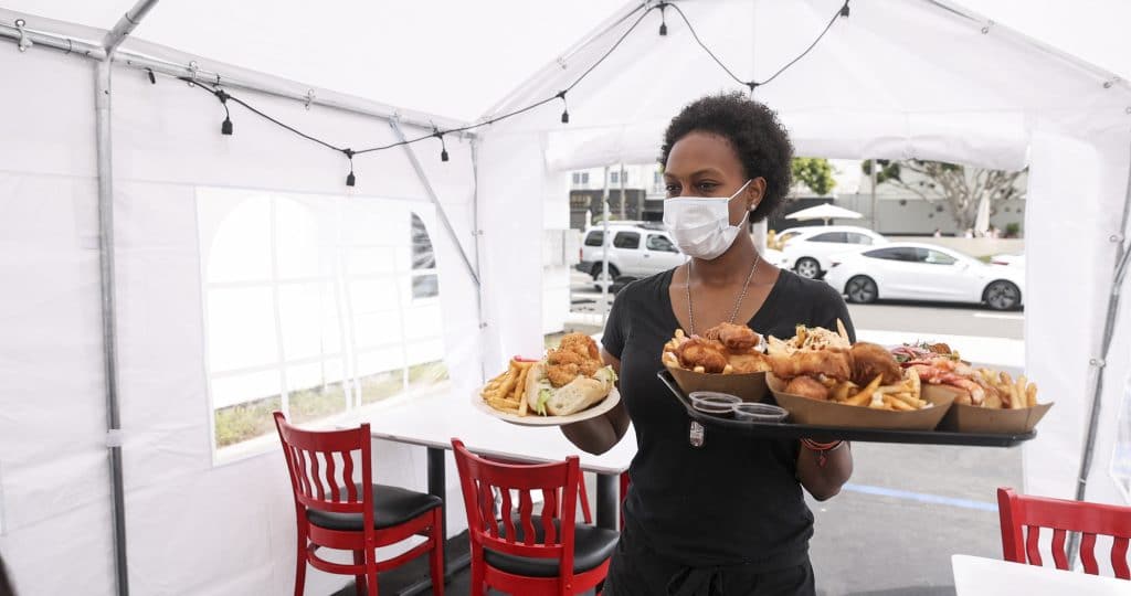 A restaurant employee serving food in an outdoor tent while wearing PPE