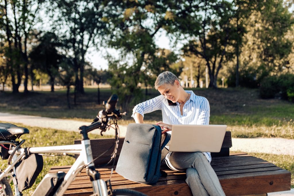 Blonde woman sitting outside with laptop on a bench
