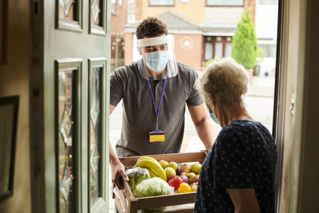 A young man visiting an elderly customer with his facemask on delivering fresh produce