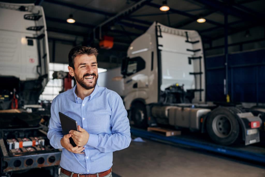 Smiling male standing in front of parked freight trucks used for LTL shipping