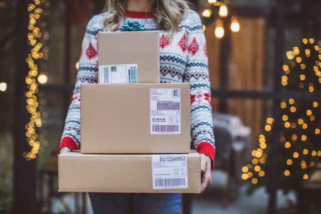 Woman in holiday sweater carry packages delivered via direct-to-consumer