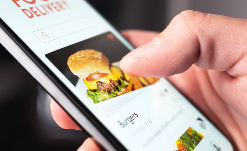 A persons hand using a phone to order a burger in a ghost kitchen