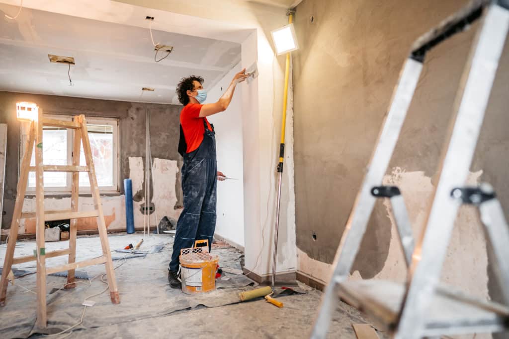 Construction worker plastering and smoothing concrete wall in room