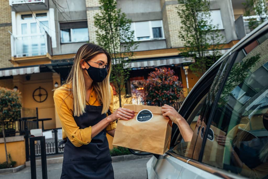 Ghost kitchen employee handing an order to customer 's vehicle parked curbside