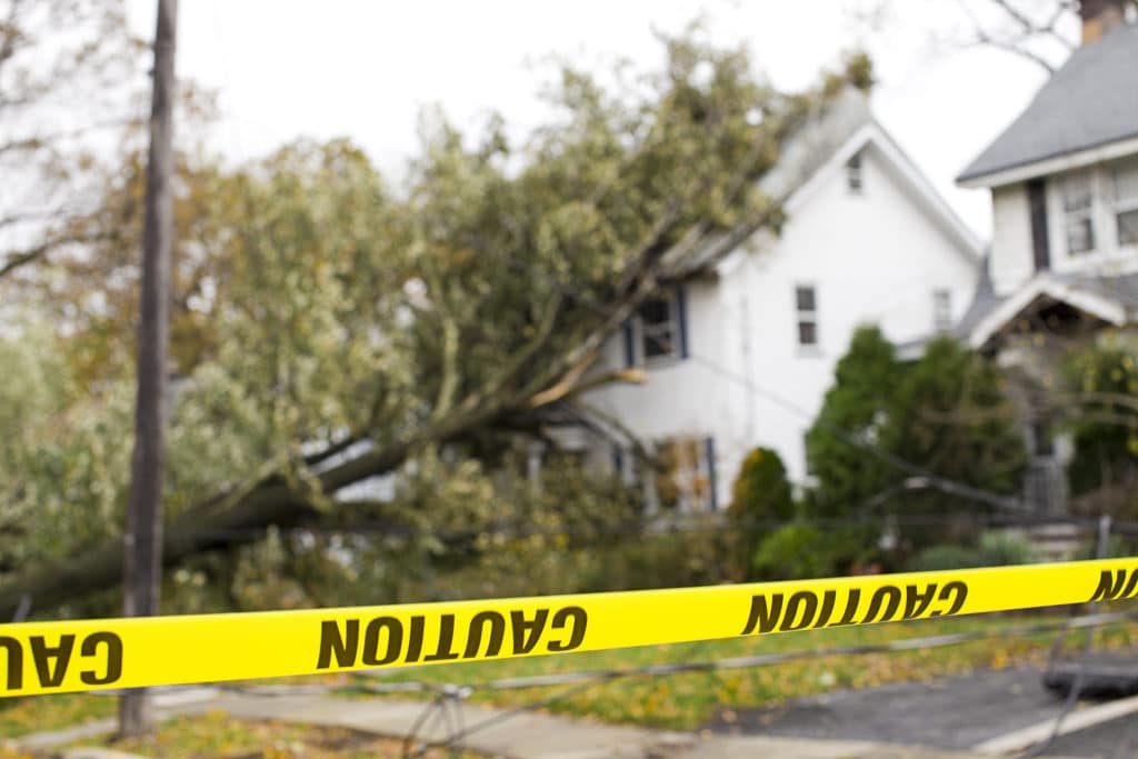 Caution tape in front of residential houses damaged by a fallen tree after a tornado