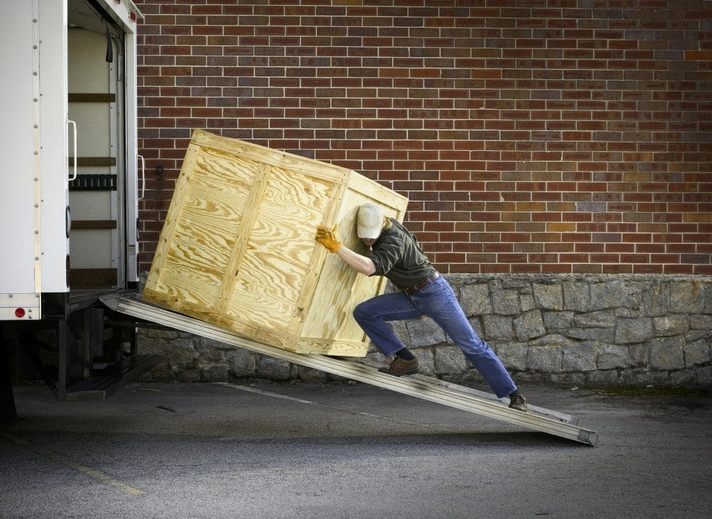 A man pushing a wood crate on a ramp into a truck