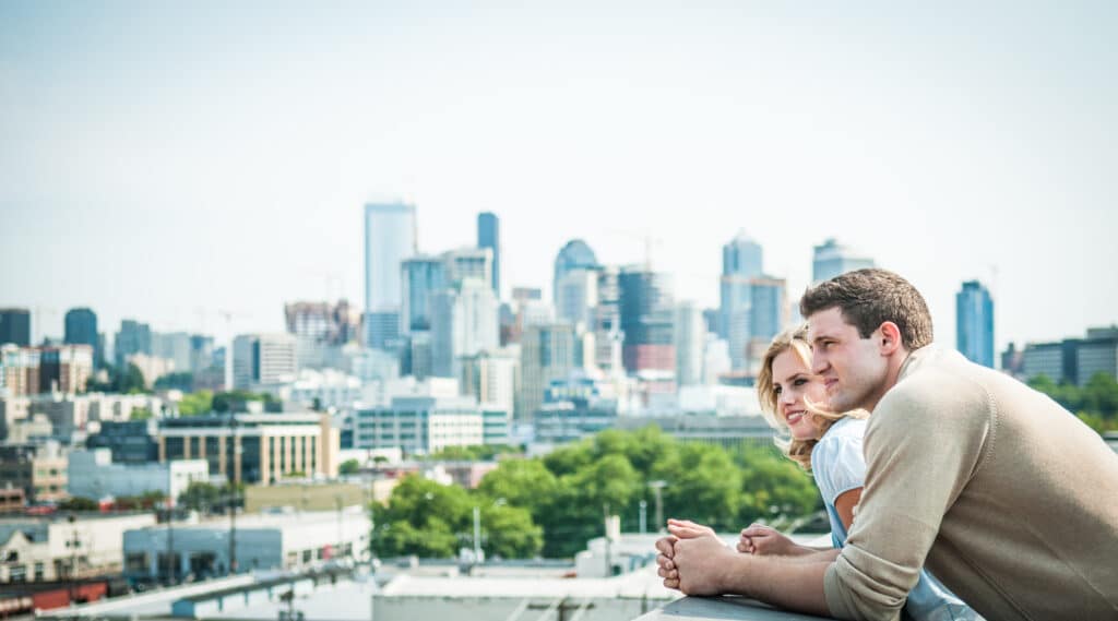 Happy couple at new home balcony with Seattle skyline in distance