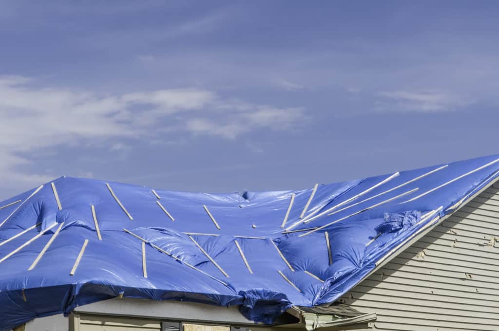 Blue plastic wrap, with wooden stays, stretched across roof of house damaged by a tornado 