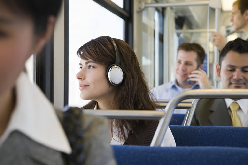 Female professional woman wearing headphones sitting on bus for commute to office