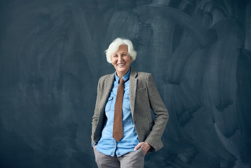 A smiling senior female professor standing in front of a black board after a faculty relocation