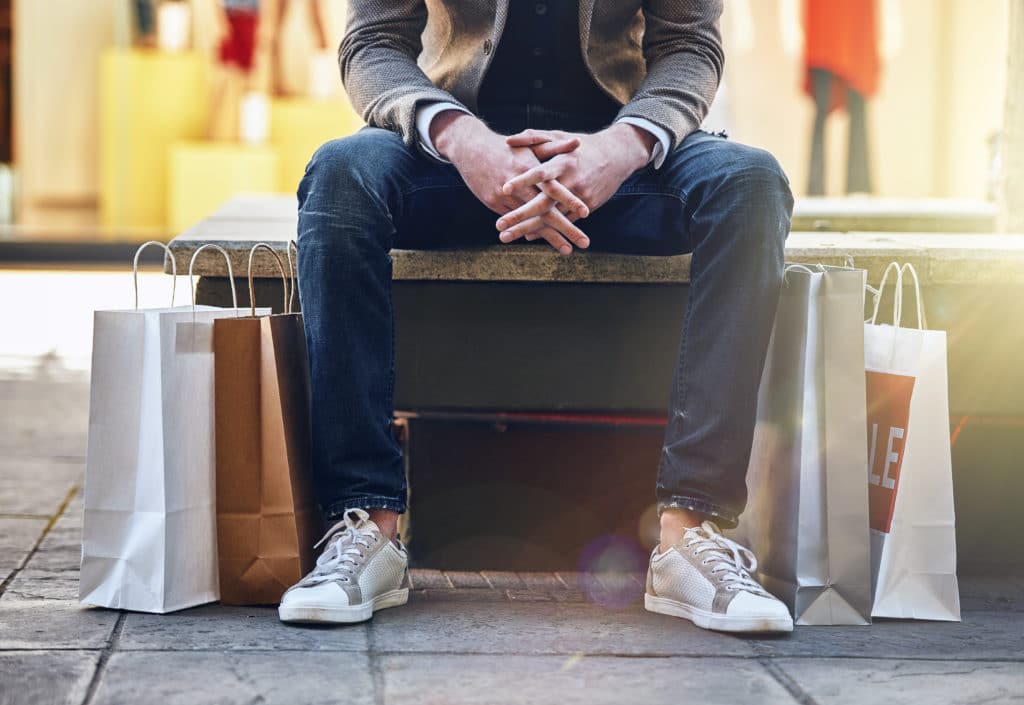 Shot of a man sitting on an outdoor bench with his shopping bags on the floor