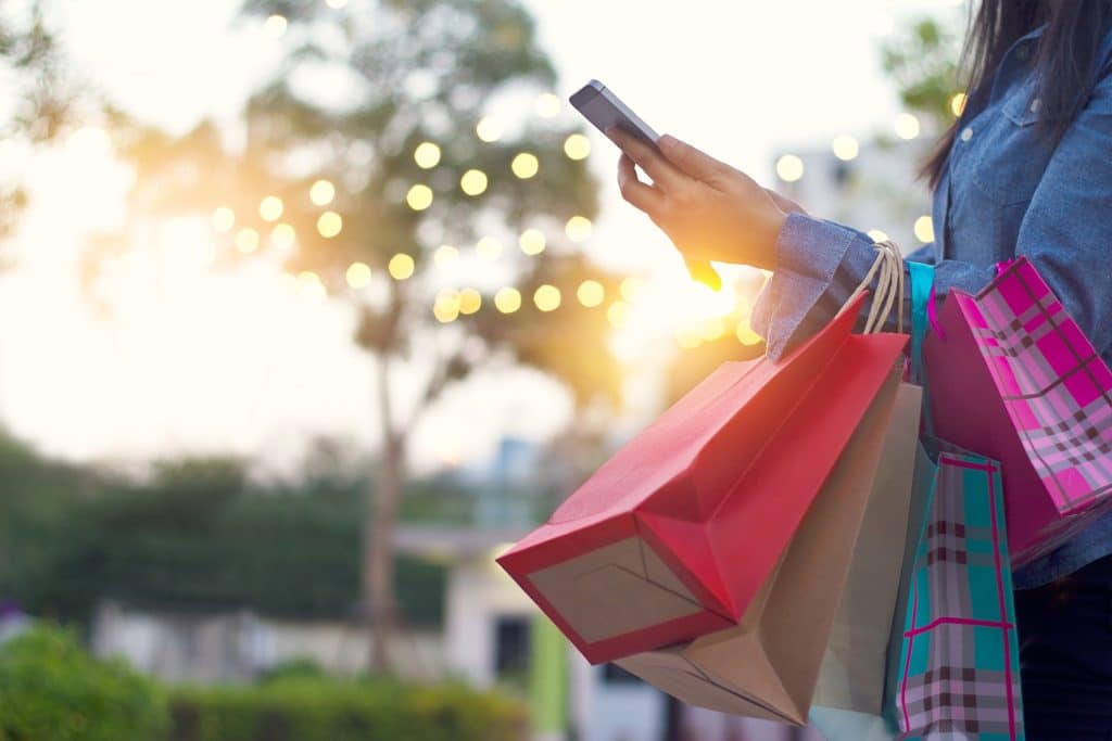 A woman holding a smartphone and shopping bags at an outdoor retail area