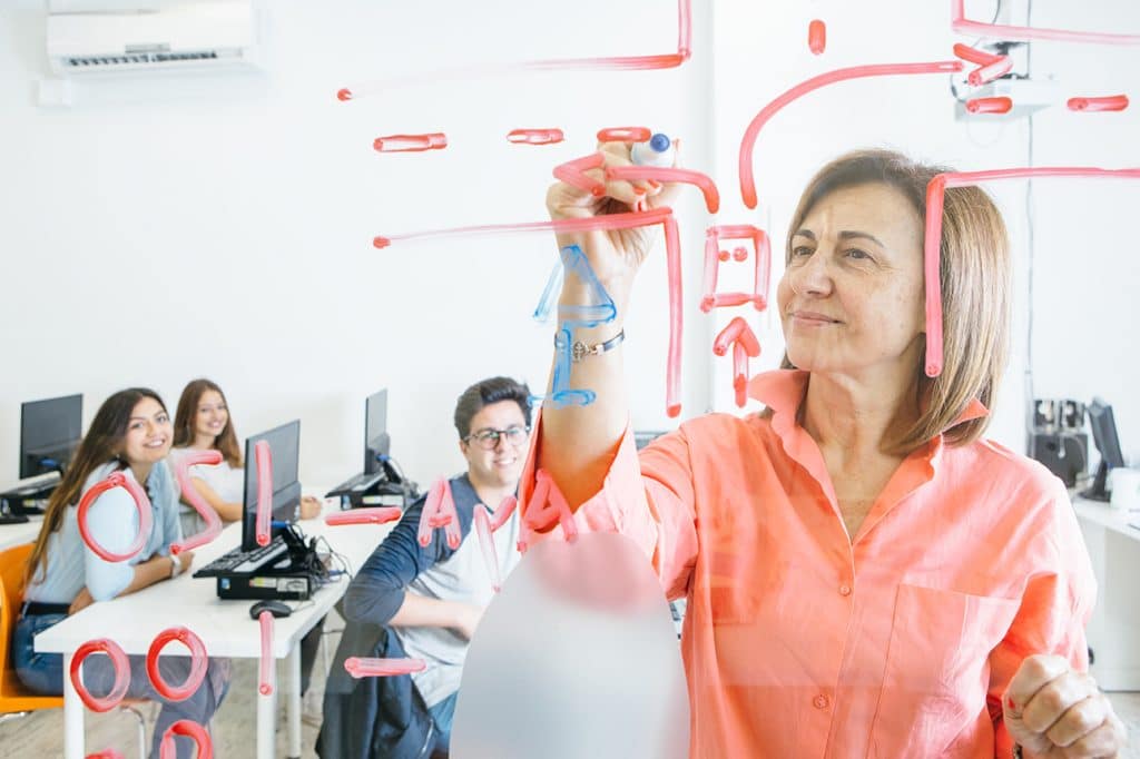 A mid-aged female professor writing on a board to teach her students sitting at their desks