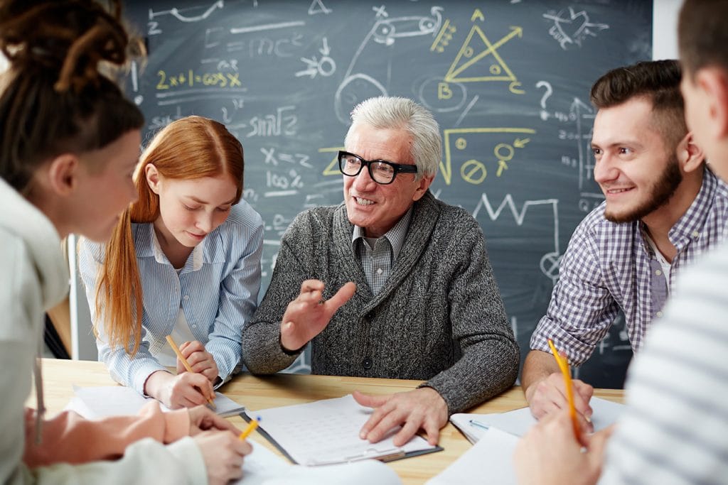 A senior male professor who had a faculty relocation sitting at a table teaching his students