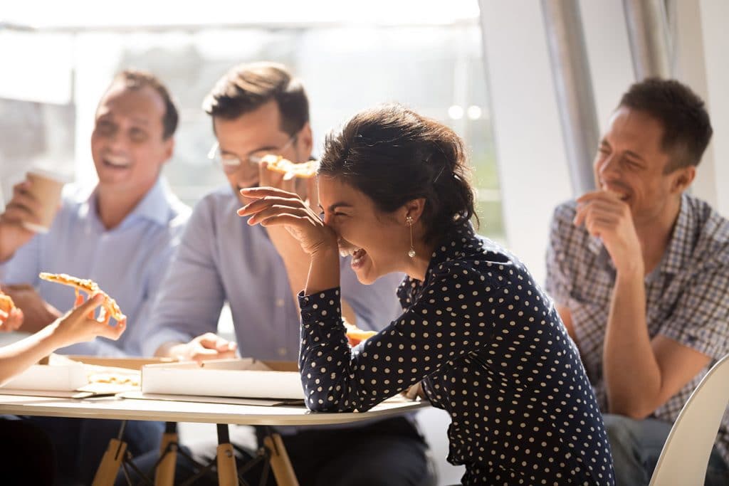 A group of employees laughing and eating pizza at a table