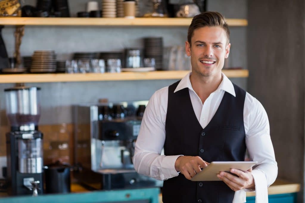 A male barista standing at a counter holding a tablet