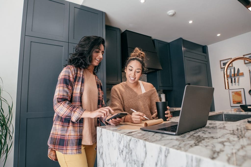 Two women discussing relocation and looking a personal laptop inside a home kitchen