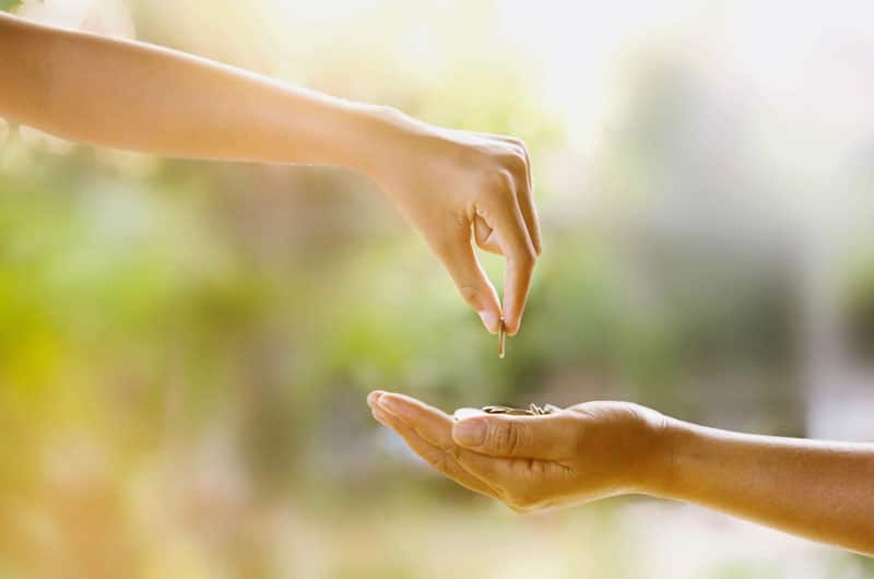 Hand passing a coin for disaster relief donations to another hand