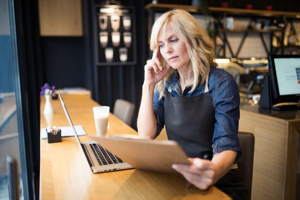 A female restaurant owner reviewing business on a laptop inside her establishment 