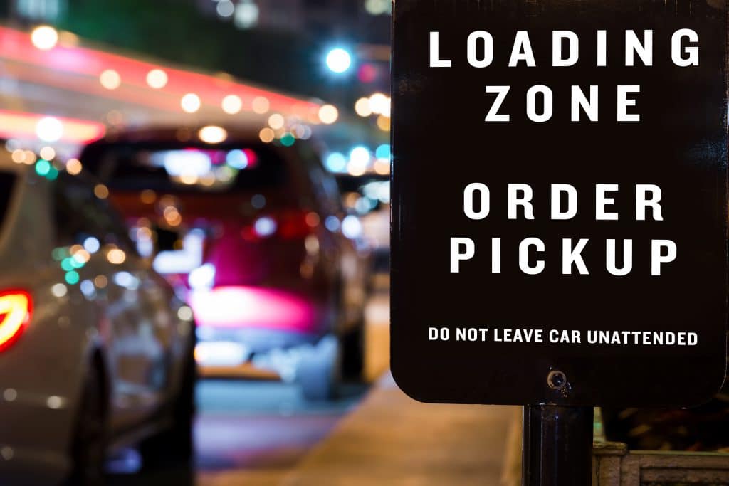 Cars in line at night at a curbside pickup area with sign