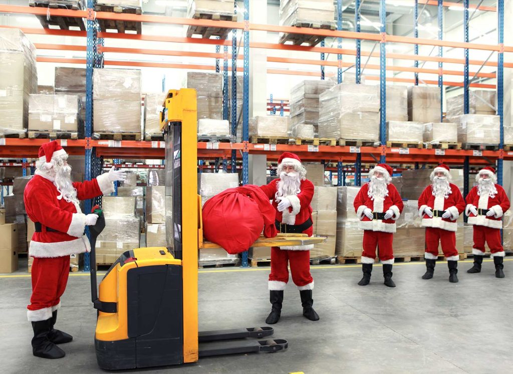 Santas in a warehouse loading gifts on a forklift