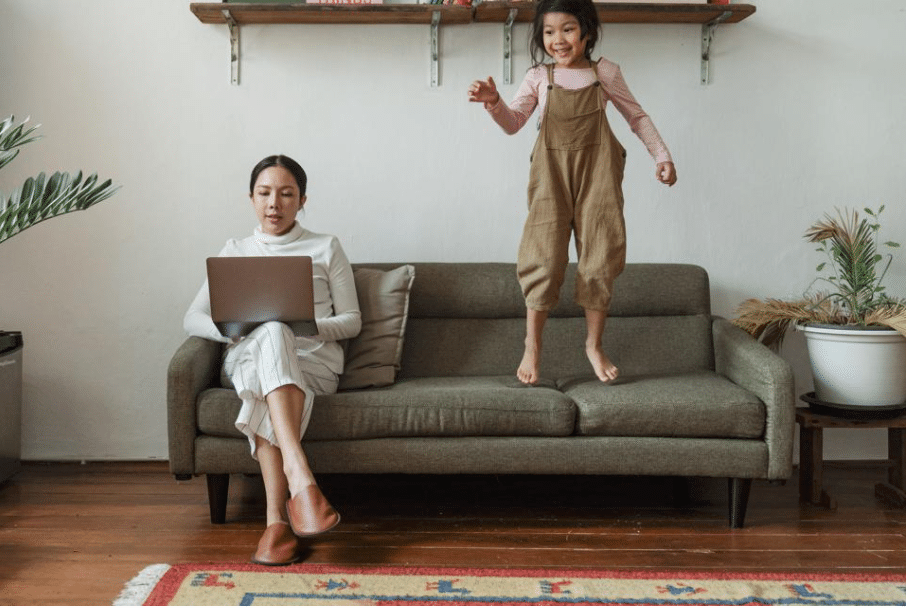 Mom working on the couch with her laptop while child bounces next to her