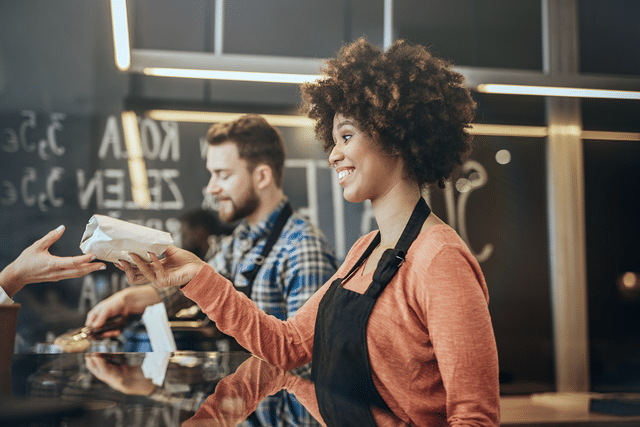 Employees at one of many fast casual restaurants handing food to a customer 