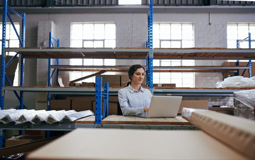 Female warehouse employee reviewing stock on a laptop