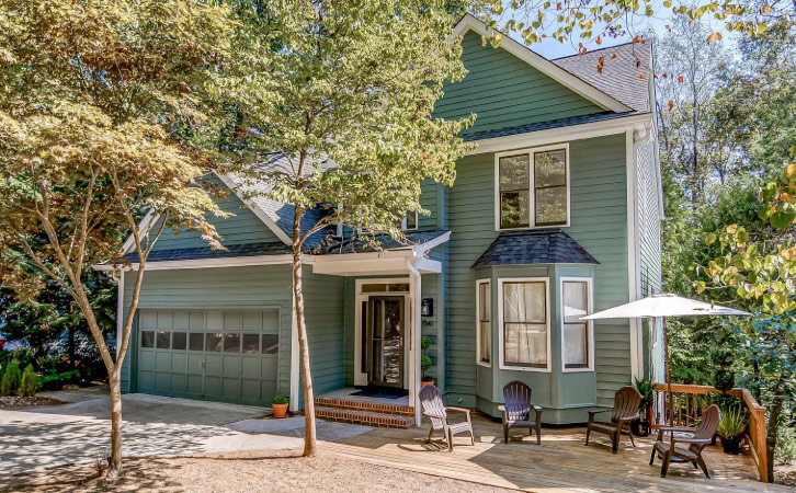 The front view of a two-story, single-family home in Carrboro, North Carolina, outside of Raleigh. The house is painted a muted shade of green which blends nicely with the surrounding woods. 