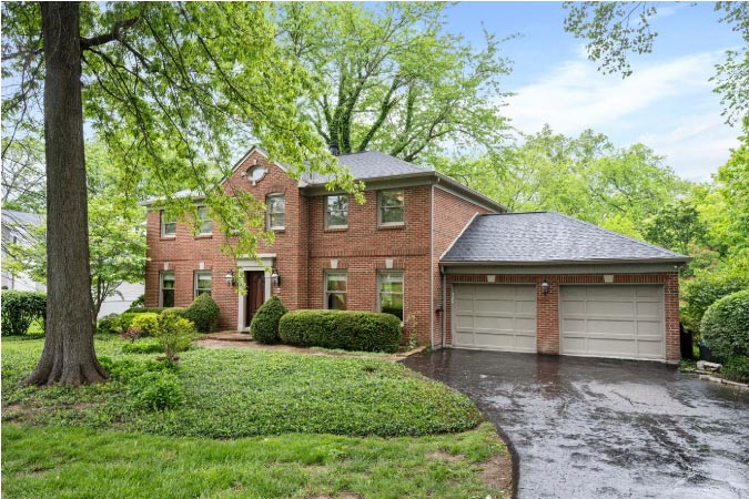A large, two-story brick home in Blue Ash, Ohio, surrounded by mature trees and a lush front yard.
