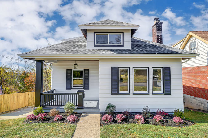A beautiful white-siding home in Fort Thomas, Kentucky, featuring a covered corner porch and a windowed attic. 