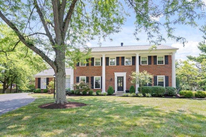 A beautiful, red-brick, Colonial-style home in Montgomery, Ohio, featuring white columns and a vast front yard.