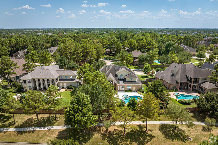 The neighborhood of Cinco Ranch in Houston, Texas. There are three mansions, two of which have pools. There are also green trees throughout. 