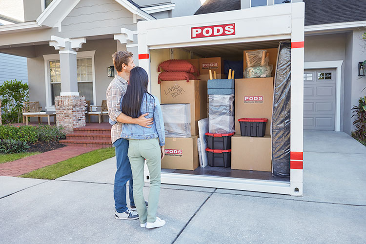 A husband and wife stand in front of a fully loaded PODS container.