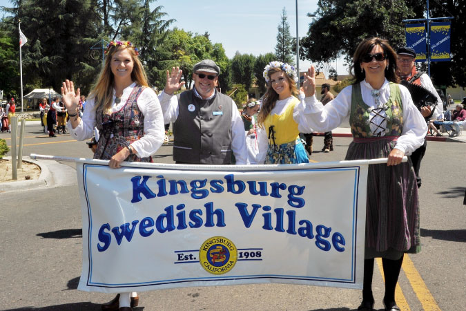 Locals dressed in festival attire hold up a sign that reads “Kingsburg Swedish Village” in Kingsburg, California