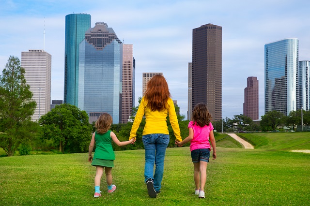 A mother walks with her two daughters, hand-in-hand, toward the Houston skyline