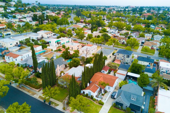 Aerial view of a neighborhood in Torrance, California, featuring a variety of home styles, green yards, and rows of cypress trees.